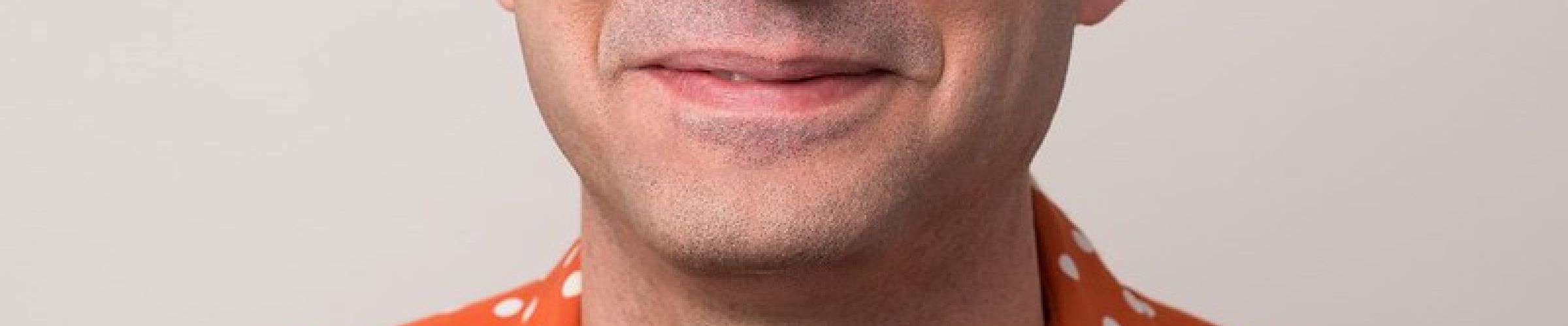 A color photo of a man with glasses smiling for a photo