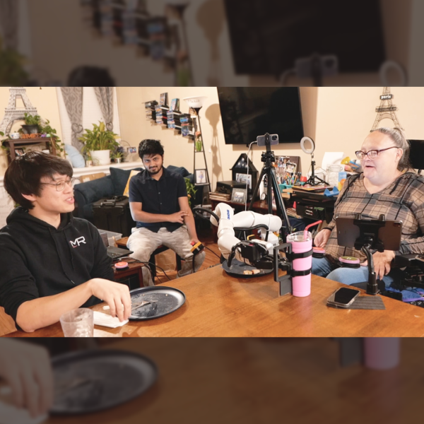 A color photo showing 3 people sitting around a dinning table with an assistive robotic devices on the table