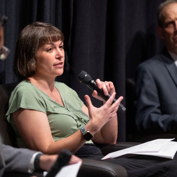 A color photo showing a woman speaking during a panel discussion.