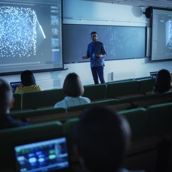 A color photo of a professor instructing students in a dark lecture hall