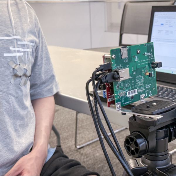 A person wearing a VitalHide prototype attached to their shirt, standing next to a wireless heart rate sensor. Provided
