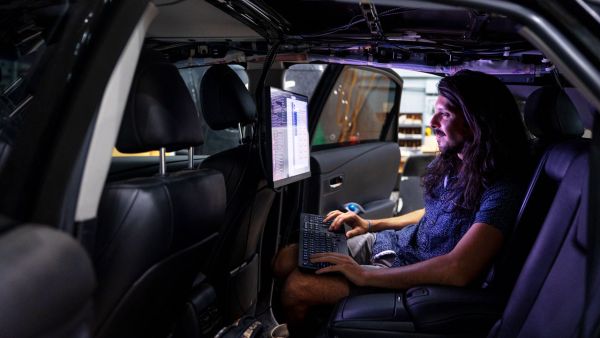 A student sits in backseat of car and looks at data collected and demonstrates some of the data collection techniques the autonomous vehicle researchers use to create their algorithms.