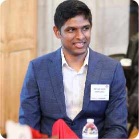 A color photo of a man smiling for a photo while seated at a table