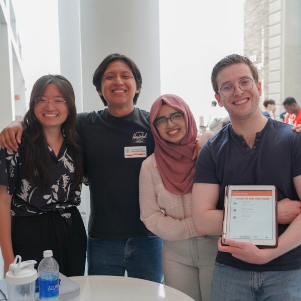 A color photo showing two women and two men smiling for a photo, with one man holding a tablet device