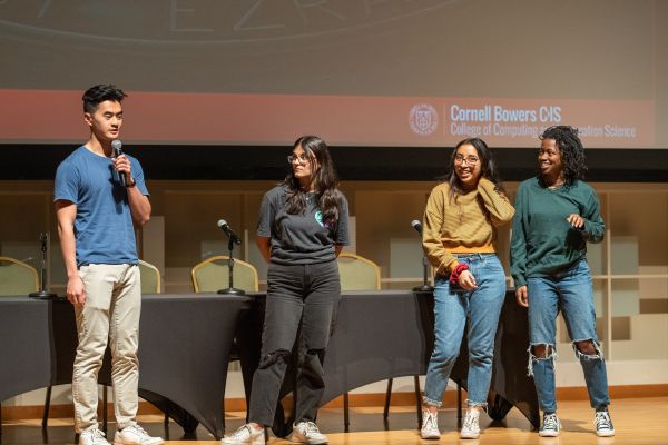 A color photo of 4 people talking to a crowd