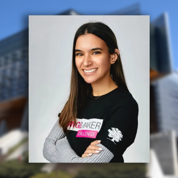 A color photo of a woman smiling for a photo with a blurred background showing Gates Hall on Cornell University's Ithaca campus