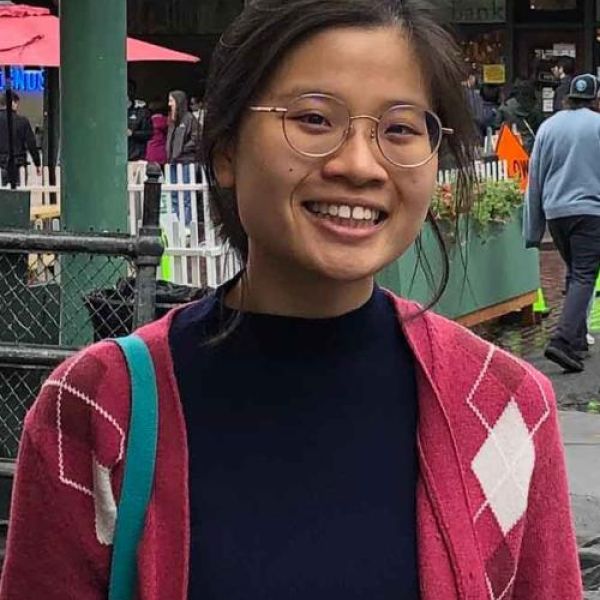 A color photo of a woman with glasses standing outside